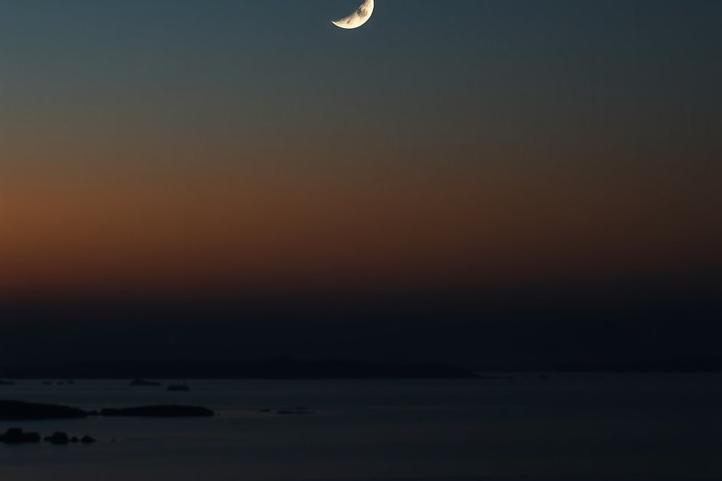 Luna creciente delgada sobre un paisaje tranquilo al anochecer
